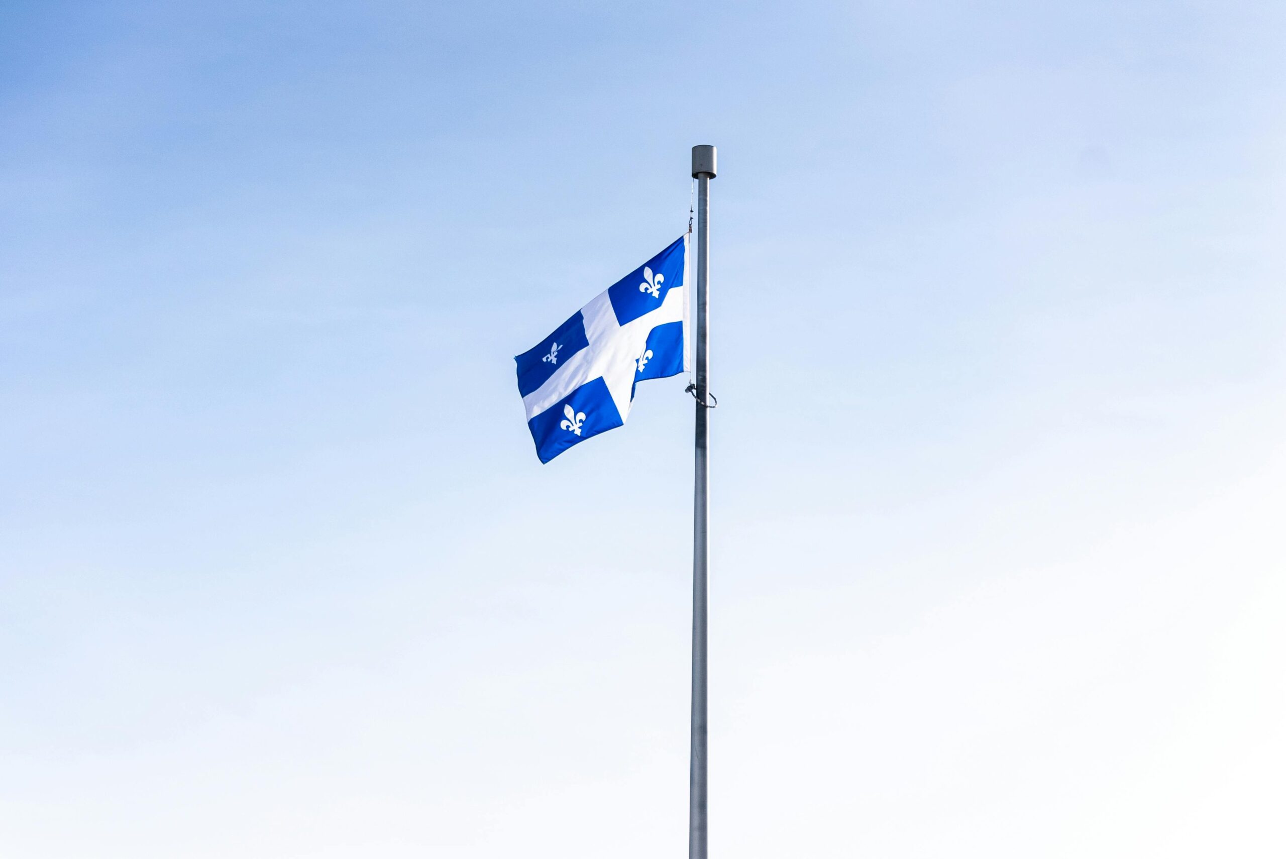 Quebec flag waving on a flagpole against a clear blue sky, symbolizing pride and identity.
