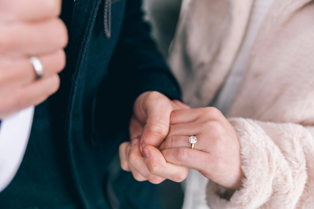 Intimate close-up of a couple holding hands, showcasing engagement and wedding rings.