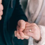 Intimate close-up of a couple holding hands, showcasing engagement and wedding rings.