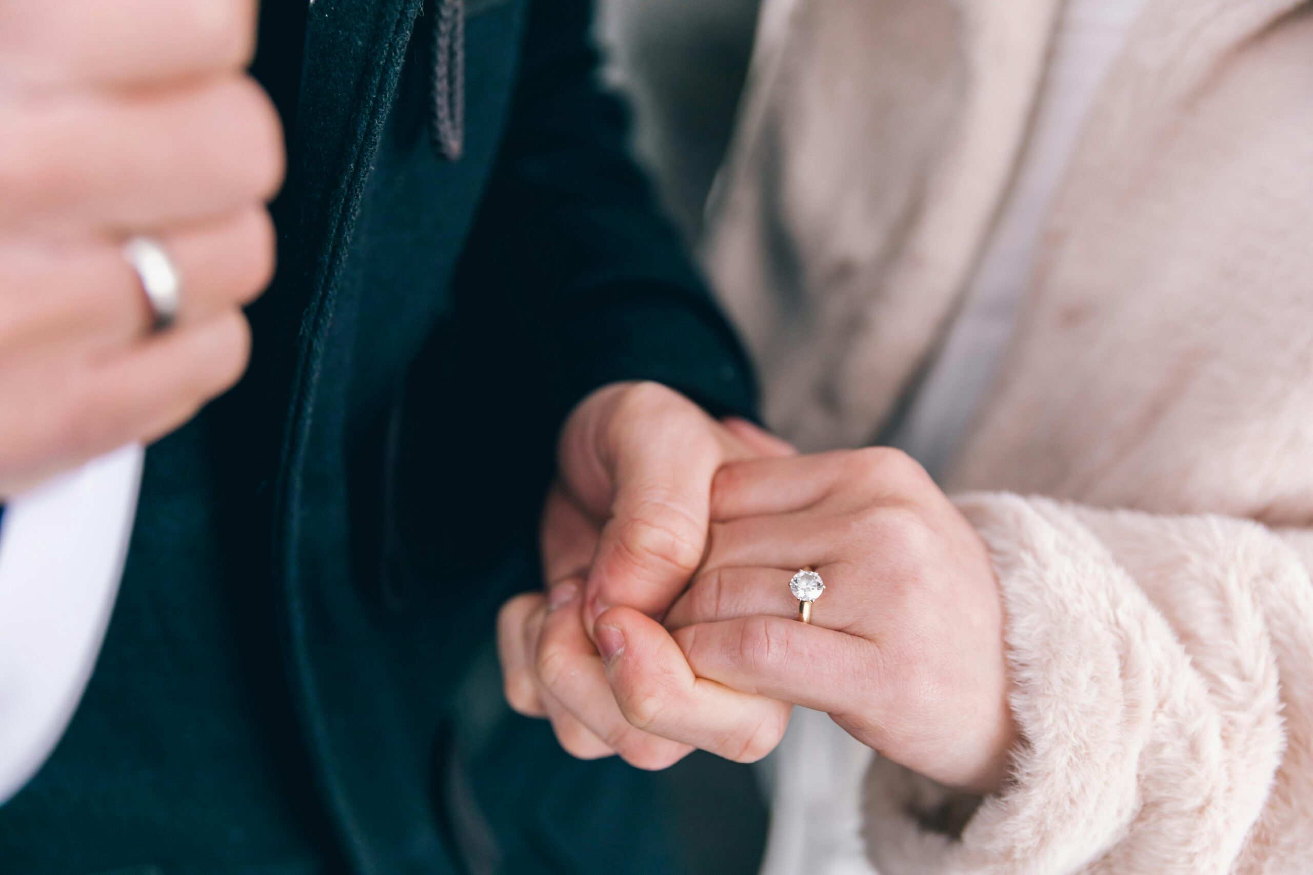 Intimate close-up of a couple holding hands, showcasing engagement and wedding rings.