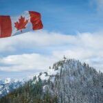 A scenic view of the Canadian flag waving with snow-covered mountains in the background.