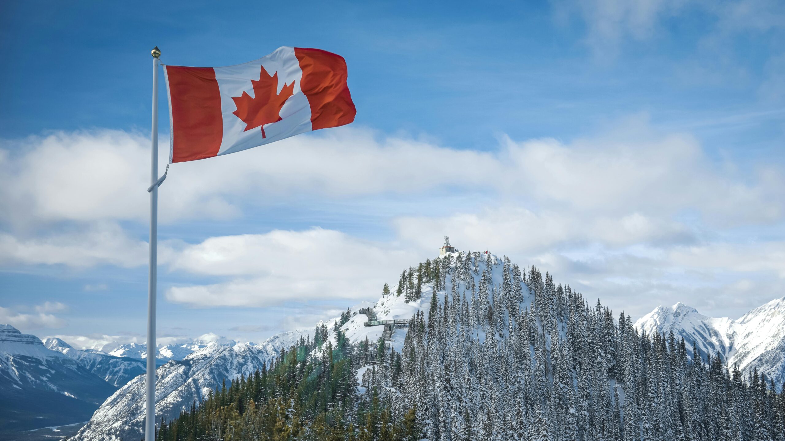 A scenic view of the Canadian flag waving with snow-covered mountains in the background.